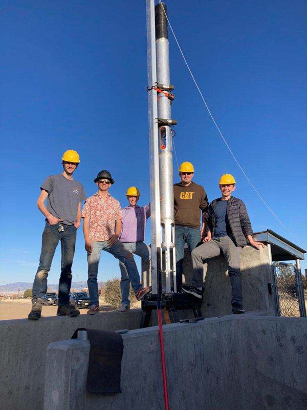 5 people in hardhats standing by a rocket